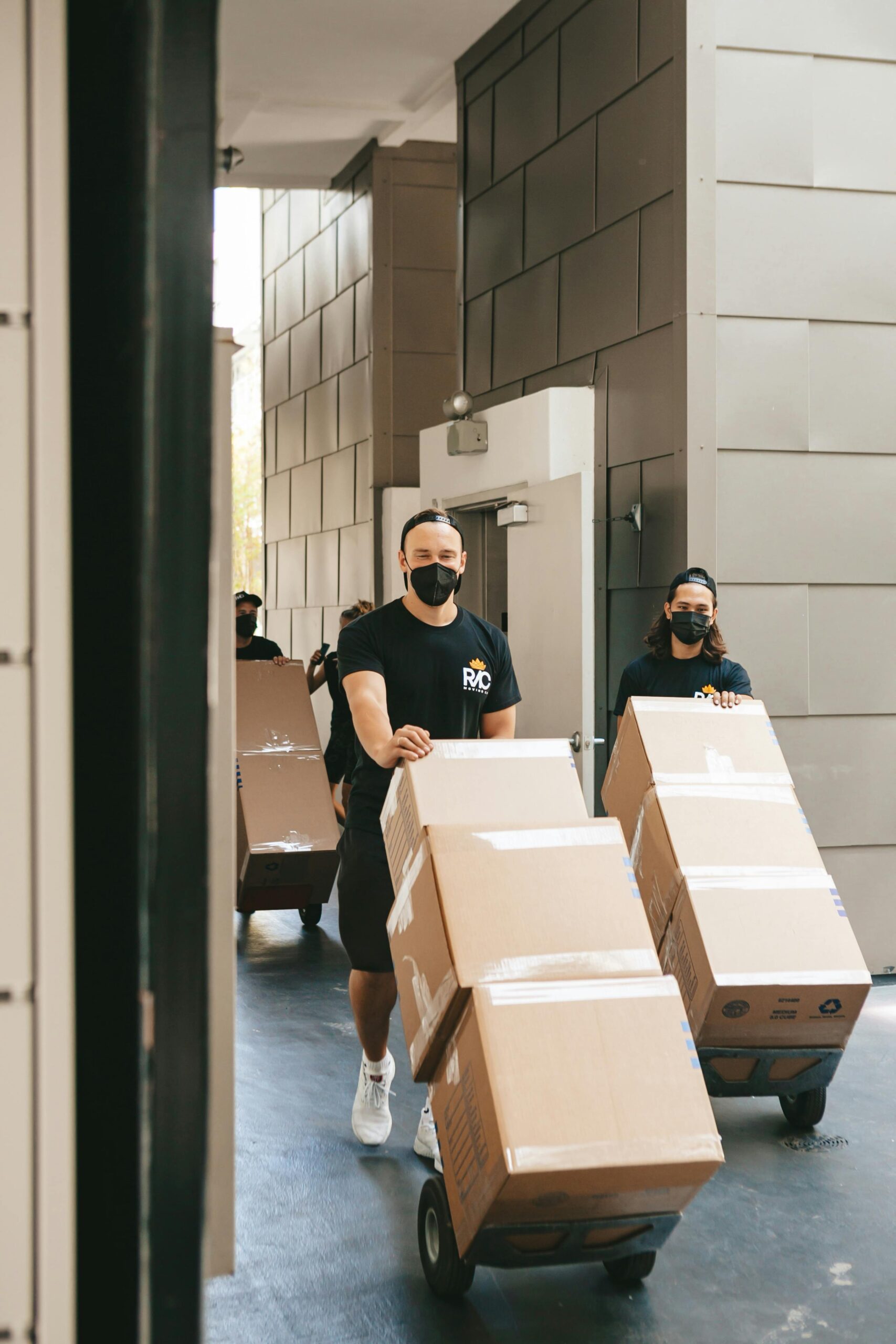 Masked workers transport boxes in an urban alleyway for delivery or relocation.