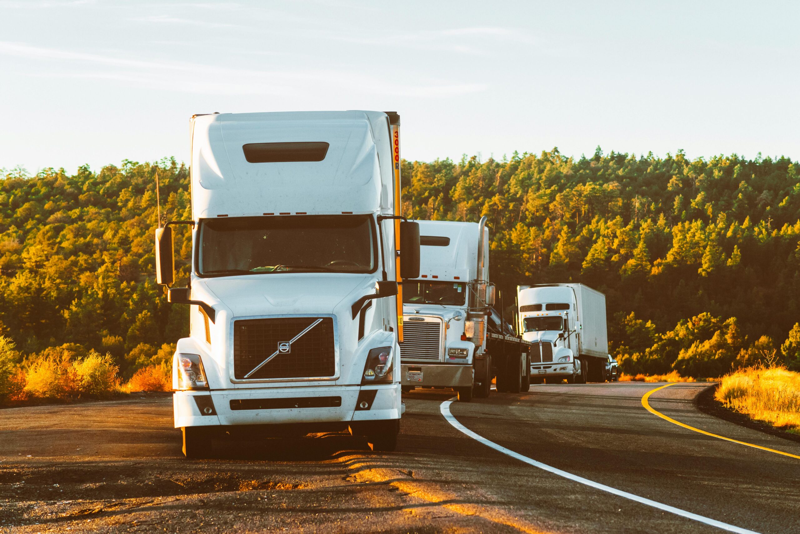 Three semi trucks driving on a highway through a forested landscape in Arizona.